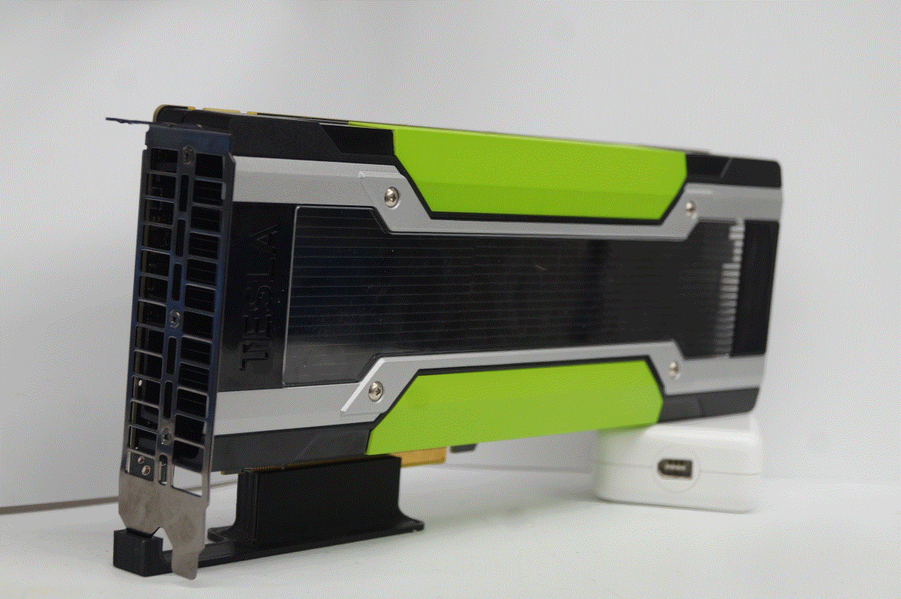 An NVIDIA Tesla K80 Graphics Card. It is rectangular, with a metal bracket at one end for securing to a computer case and a power connector at the other end. The circuit board is entirely covered with a large black heatsink, which in turn is covered by a black, green, and translucent shroud to direct airflow. There is a noticeable lack of video out ports and fans on the card.